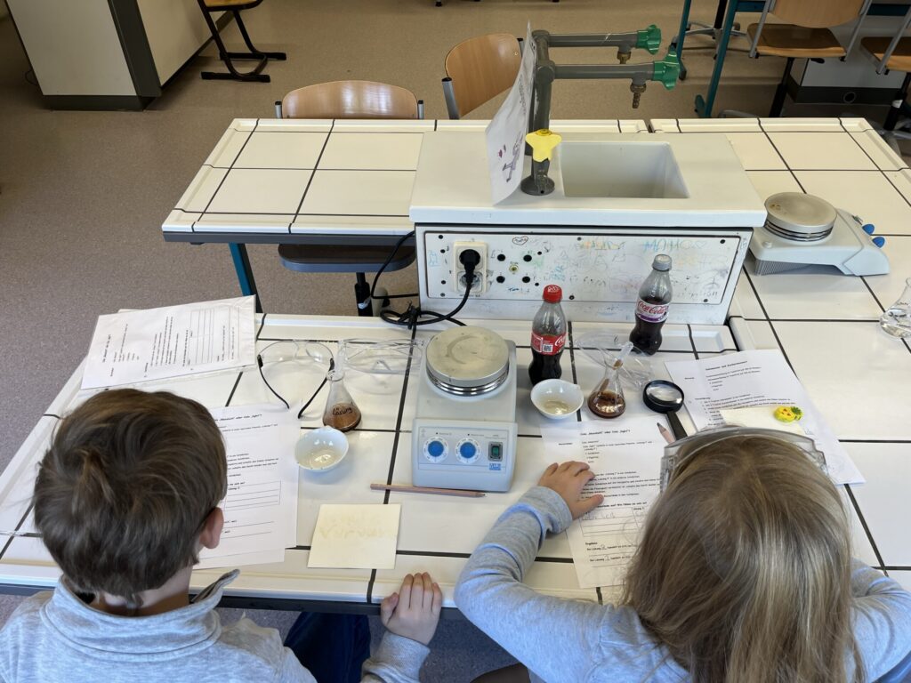 Zwei Schüler arbeiten an einem Tisch im Labor mit Experimentiermaterialien.