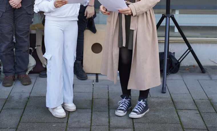 Zwei Mädchen halten Reden vor Stolpersteinen auf dem Gehweg.
