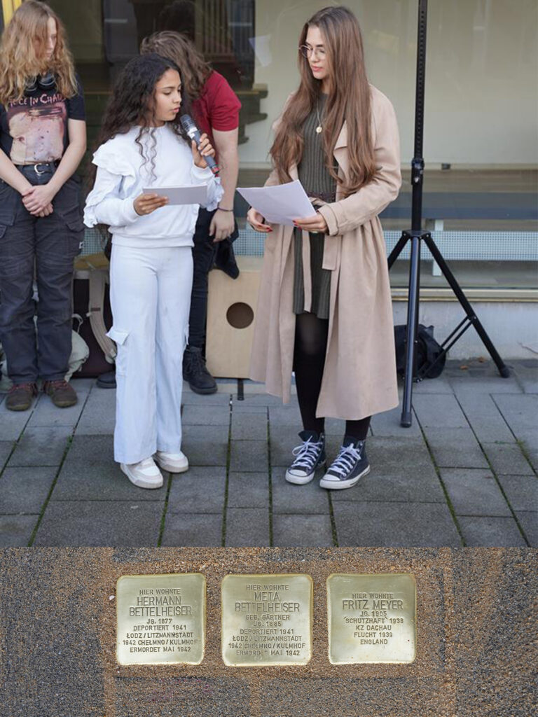 Zwei Mädchen halten Reden vor Stolpersteinen auf dem Gehweg.