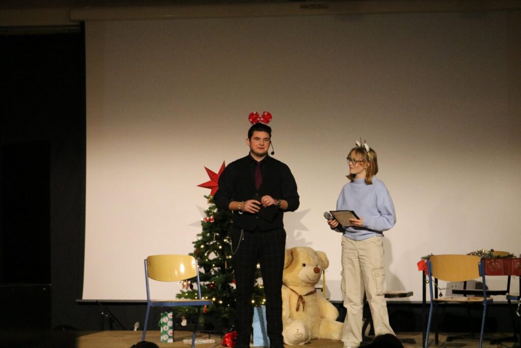 Zwei Personen stehen auf einer Bühne vor einem Weihnachtsbaum.