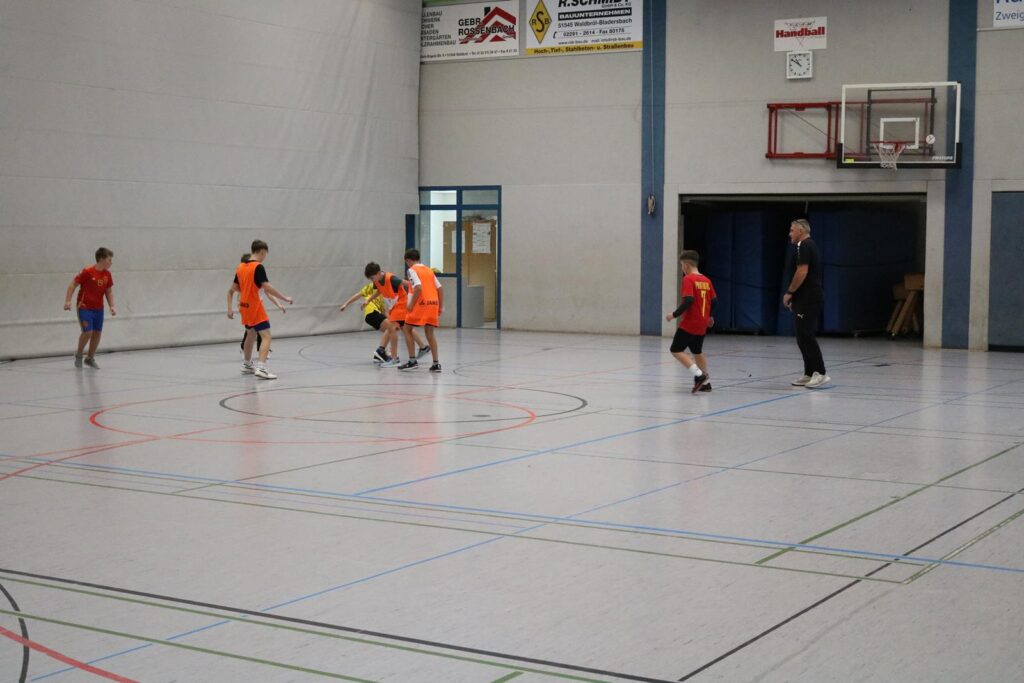 Sechs Schüler spielen in einer Sporthalle Basketball.