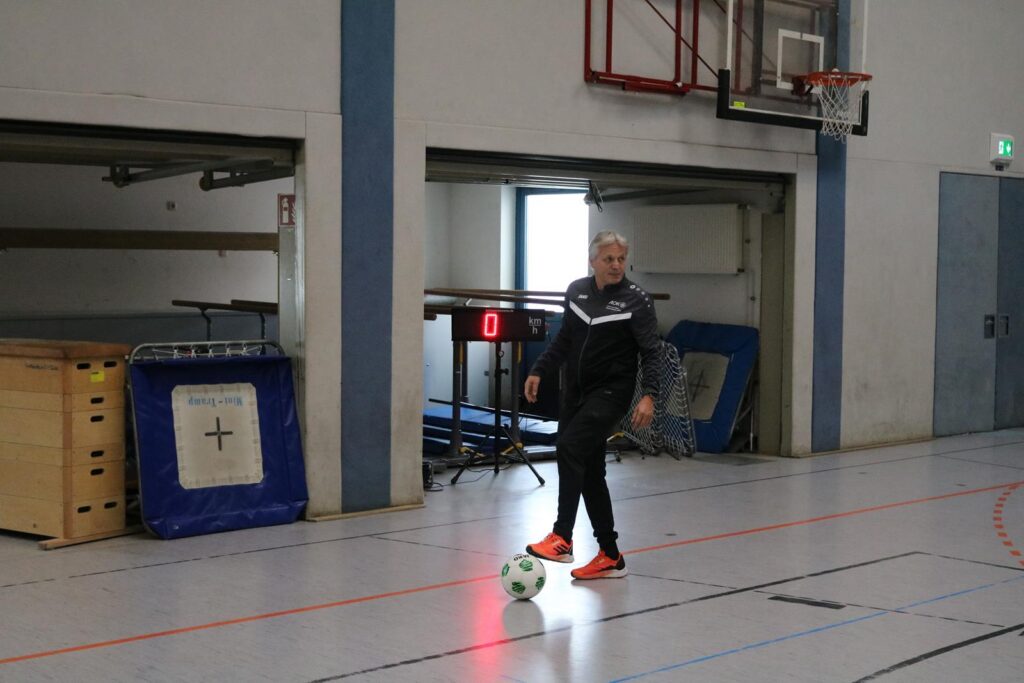 Ein Trainer steht in einer Sporthalle mit einem Fußball.