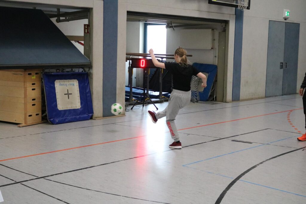 Mädchen kickt einen Fußball in einer Turnhalle.
