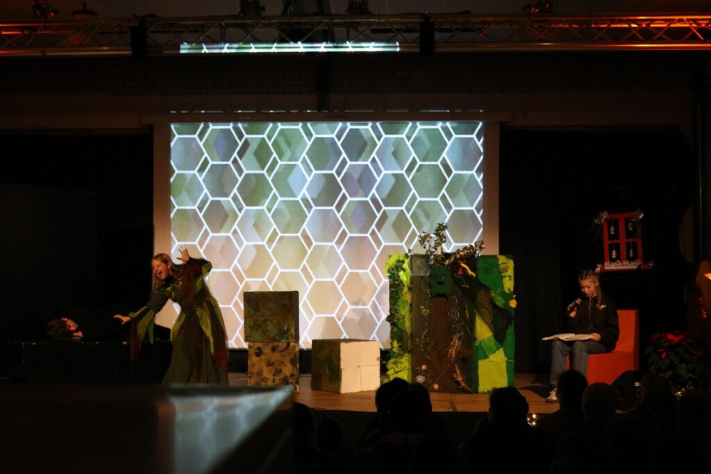 Aufführung auf der Bühne mit Projektionen und Schauspielern in Kostümen.
