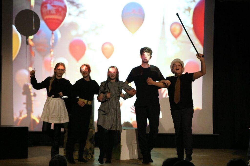 Fünf Performer auf einer Bühne, vor einer Projektion mit Heißluftballons.