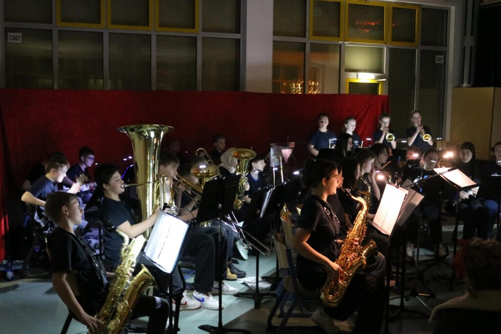 Schülerinnen und Schüler spielen in einem dunklen Saal in einem Blasorchester.