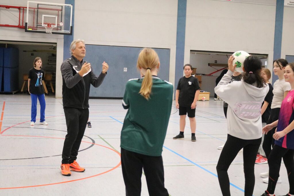 Sportliche Übung in der Halle mit Trainer und Schülerinnen.