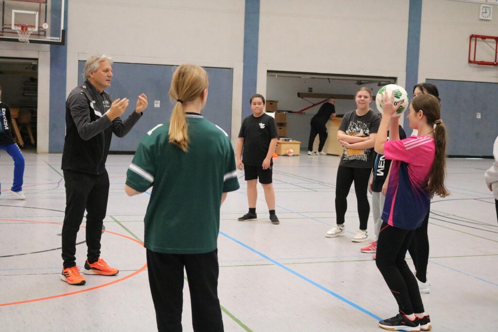 Trainingseinheit in der Sporthalle mit mehrerenTeilnehmern und einem Trainer.