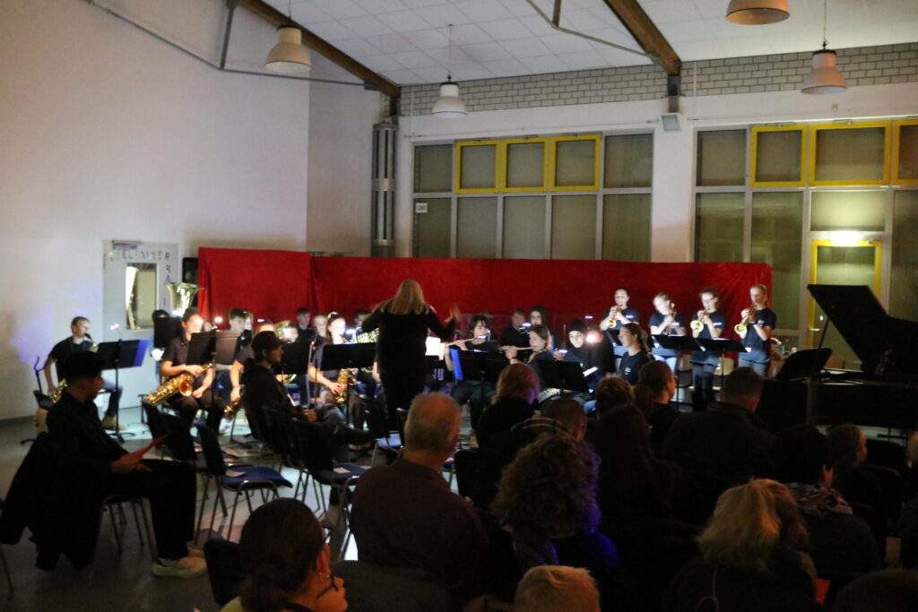 Schülerinnen und Schüler spielen im Schulkonzert, Publikum schaut zu.