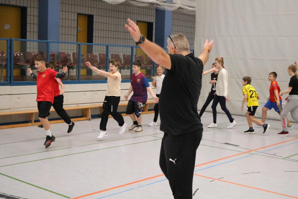 Kinder und ein Trainer in einer Turnhalle beim Sportübungen.