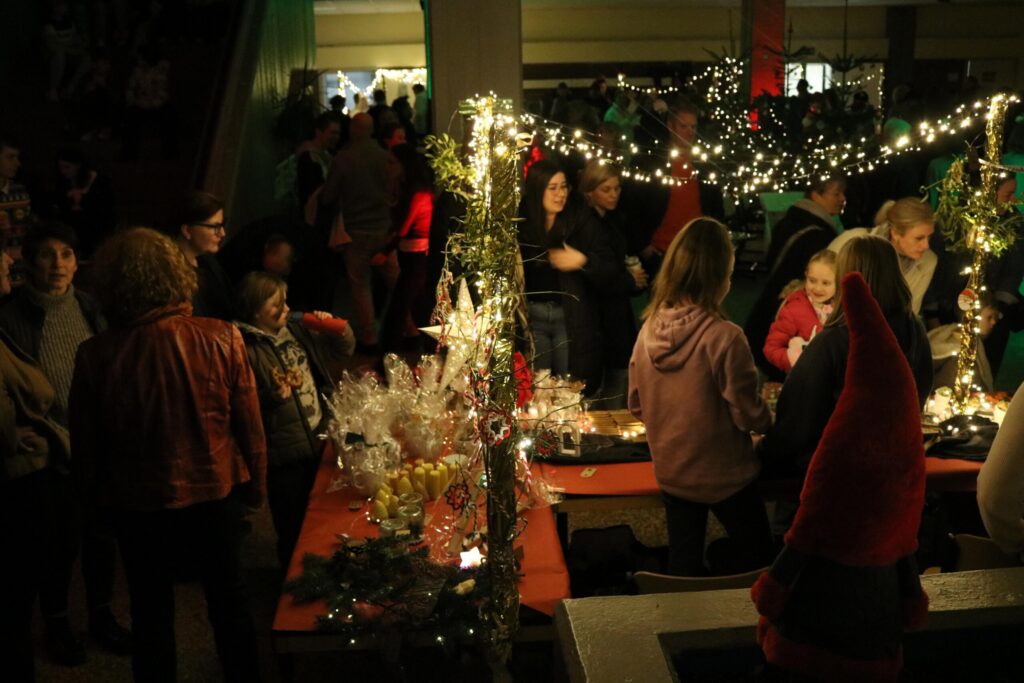 Besucher auf einem Weihnachtsmarkt mit Ständen und Lichtern.