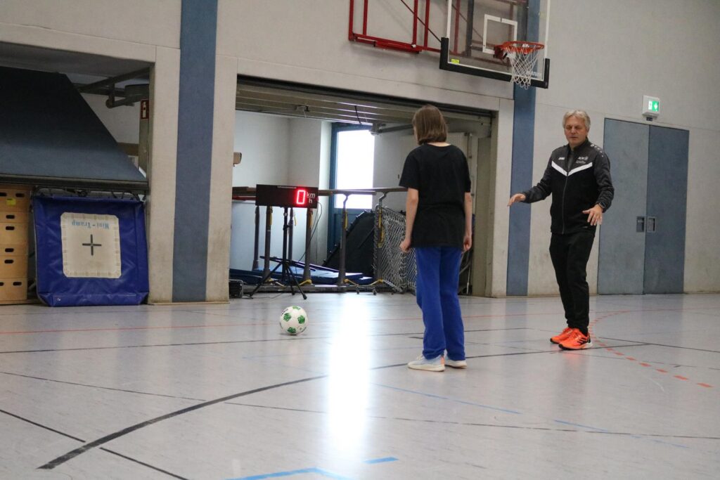 Ein Trainer zeigt einem Schüler, wie man Fußball spielt, in einer Turnhalle.