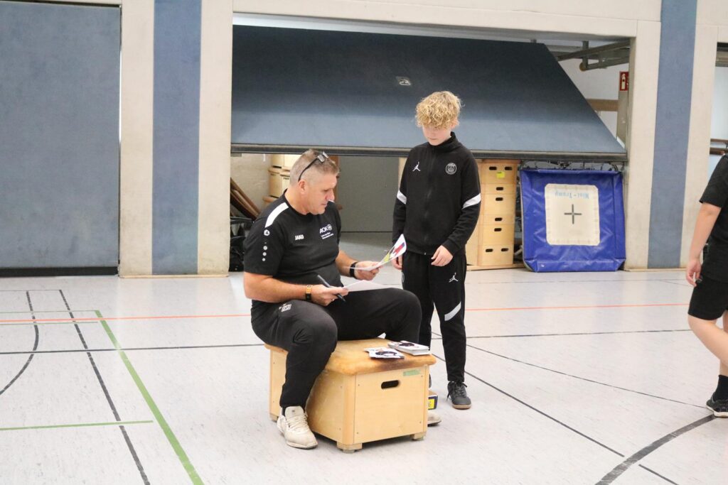 Ein Trainer sitzt auf einer Kiste und bespricht etwas mit einem Jugendlichen.