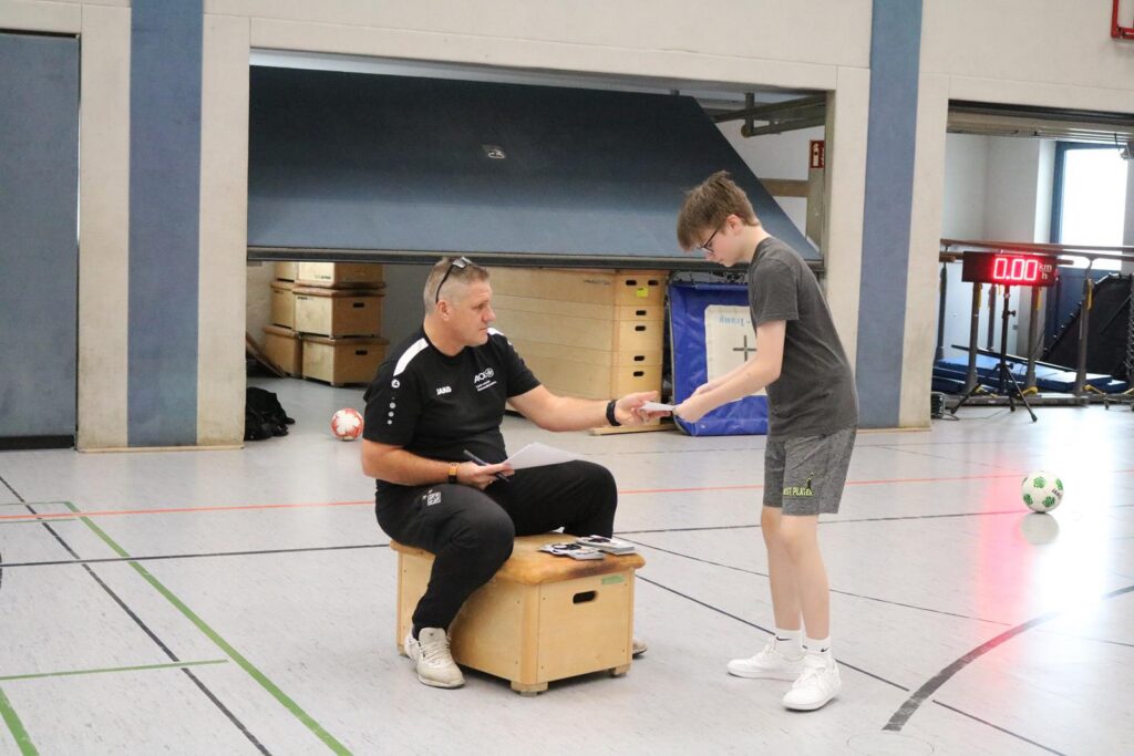 Ein Trainer sitzt auf einer Kiste und überprüft die Ausrüstung eines jungen Sportlers.