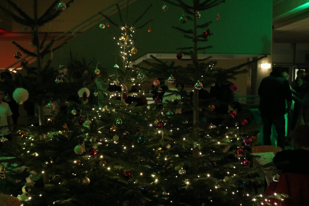 Weihnachtsbaum mit Lichtern und Dekoration, im Hintergrund Menschen und festliche Atmosphäre.