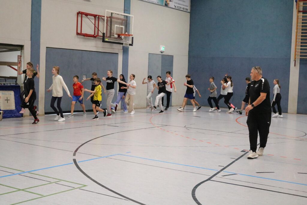 Schülerinnen und Schüler joggen in einer Sporthalle.