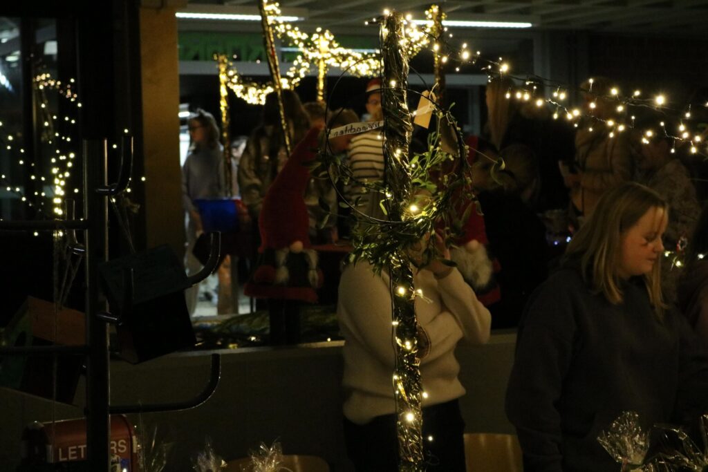 Menschen stehen an einem Weihnachtsmarktstand mit Lichtern und Dekorationen.