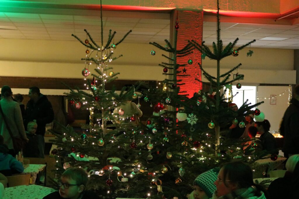 Weihnachtsbaum mit Lichtern und Dekoration, Menschen im Hintergrund.
