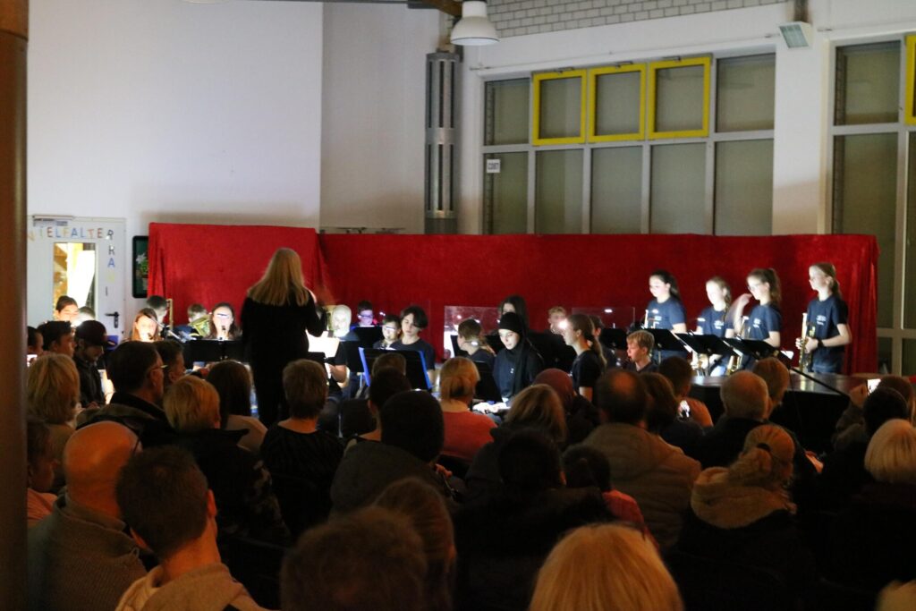 Schüler führen ein Konzert vor Publikum auf, im Hintergrund eine rote Bühne.