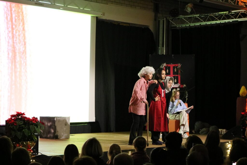 Theateraufführung mit mehreren Personen auf der Bühne und einer Kulisse.
