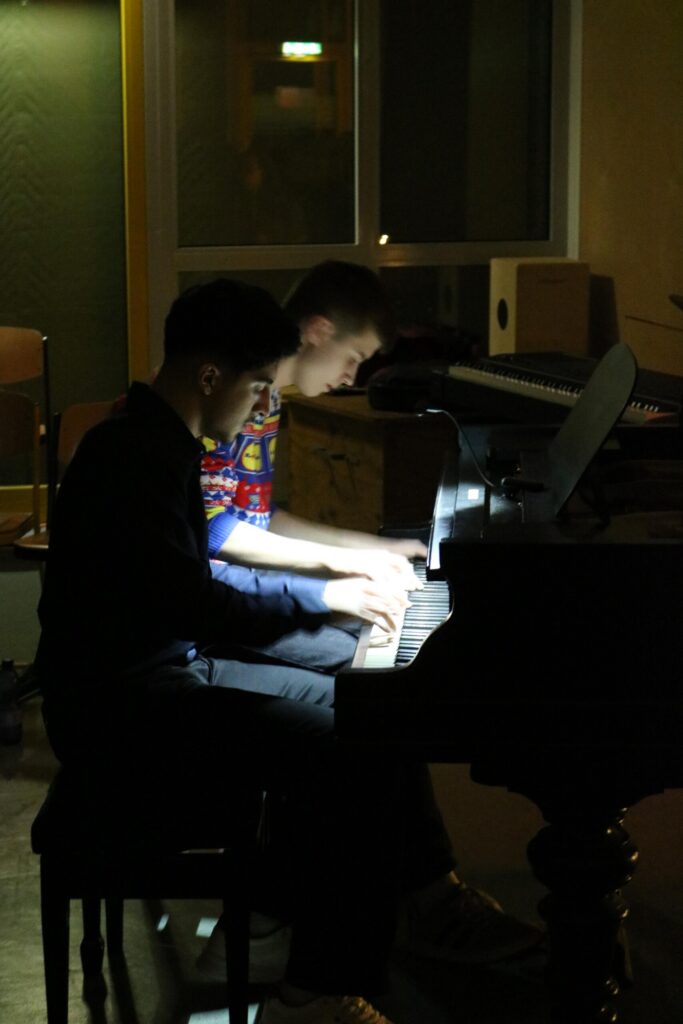Zwei Personen spielen gleichzeitig Klavier in einem dunklen Raum.