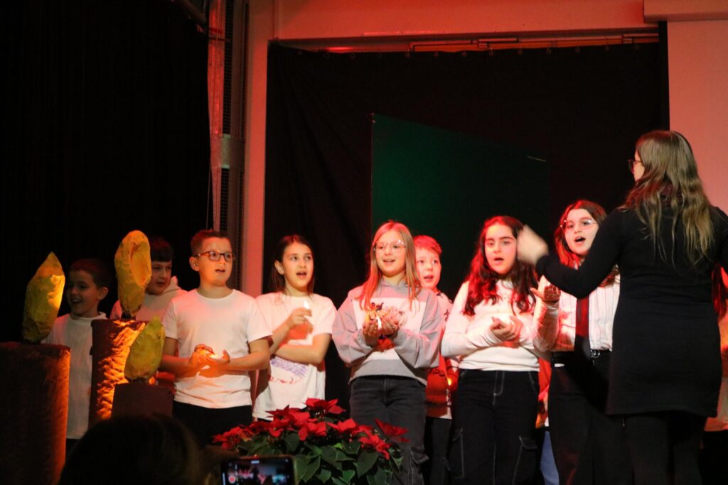Schüler singen auf einer Bühne, umgeben von dekorativen Elementen.