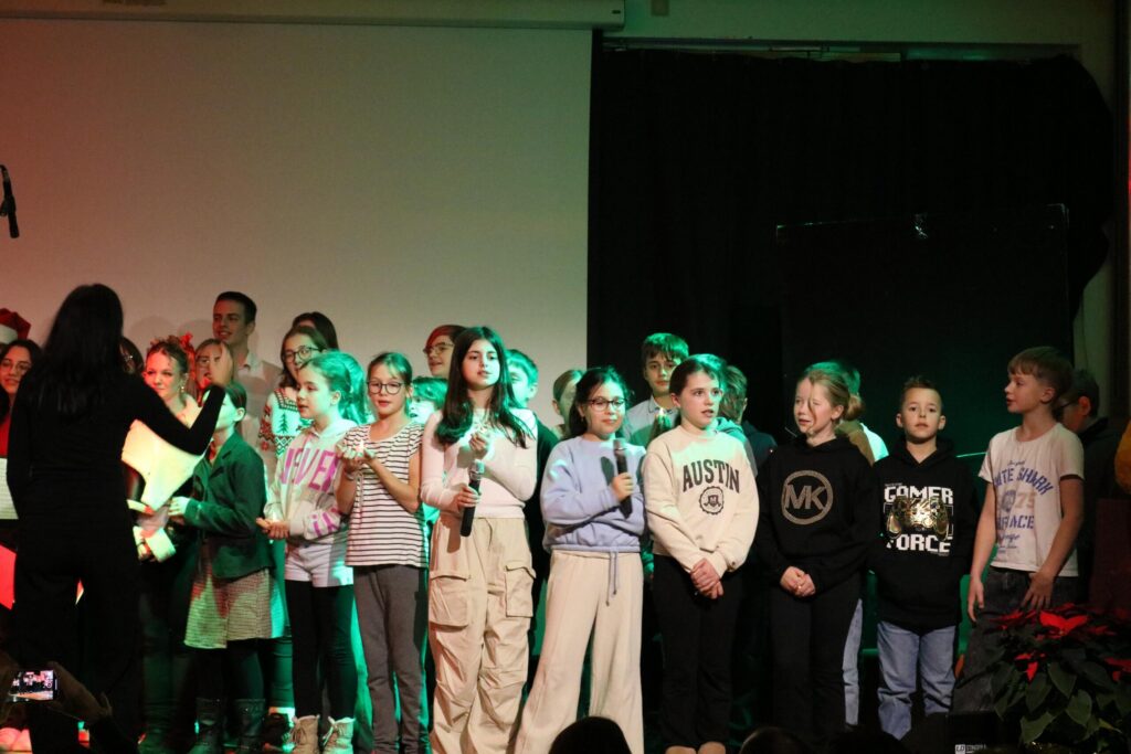 Schülerinnen und Schüler stehen auf der Bühne und singen gemeinsam.