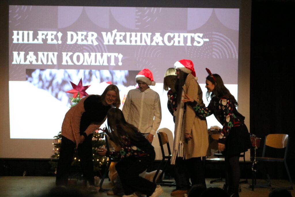 Aufführung mit mehreren Personen in festlicher Kleidung auf einer Bühne.
