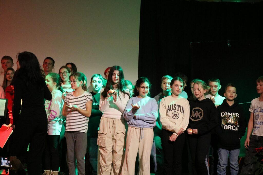 Schülerinnen und Schüler stehen auf der Bühne und singen. Hintergrundbeleuchtung in Grün.