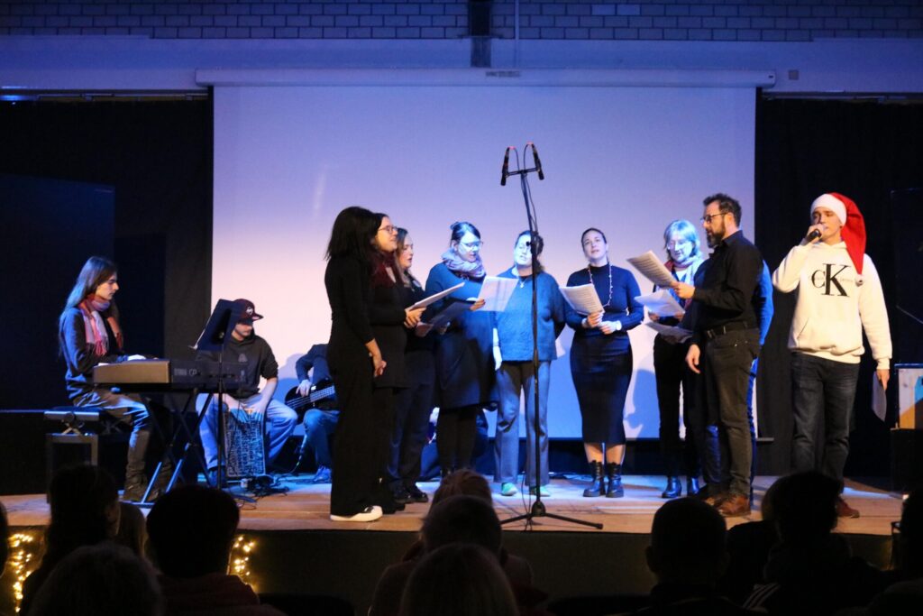 Chor und Musiker treten auf einer Bühne auf, mit Mikrofon und Klavier.