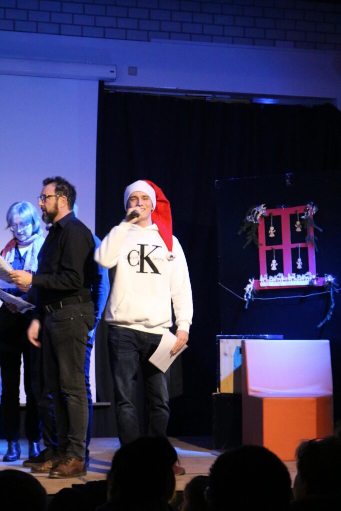Männer und Frauen auf einer Bühne, Weihnachtsmannmütze und Mikrofon.