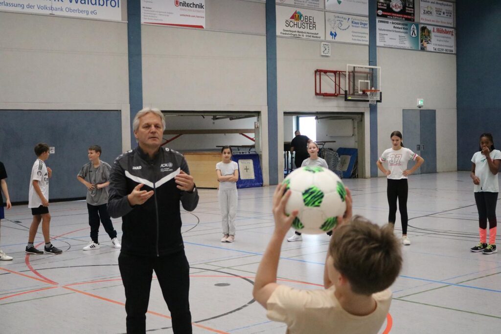 Ein Trainer erklärt Kindern das Fußballspielen in einer Sporthalle.