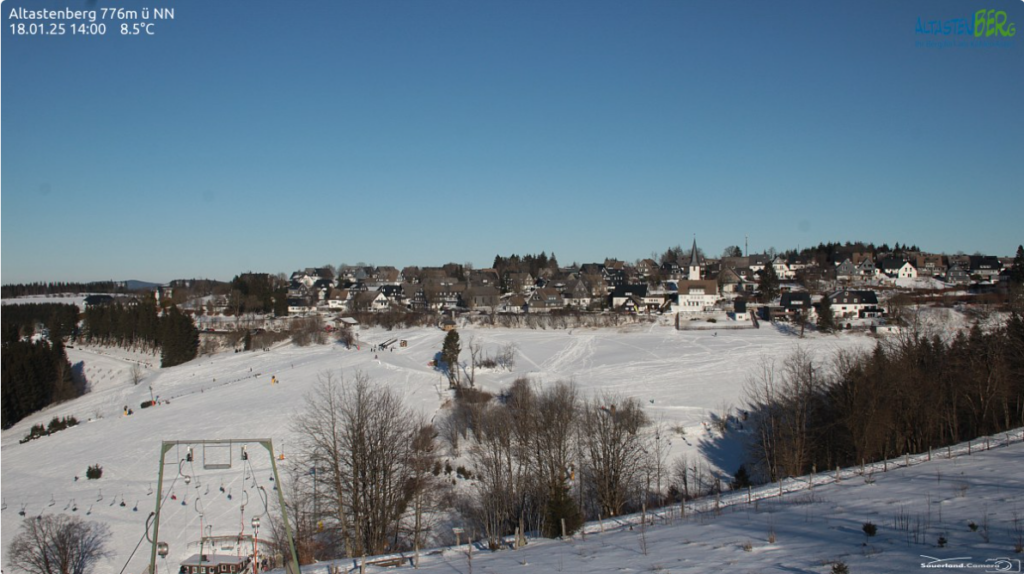 Schneebedeckte Landschaft mit einem Dorf im Hintergrund unter klarem Himmel.
