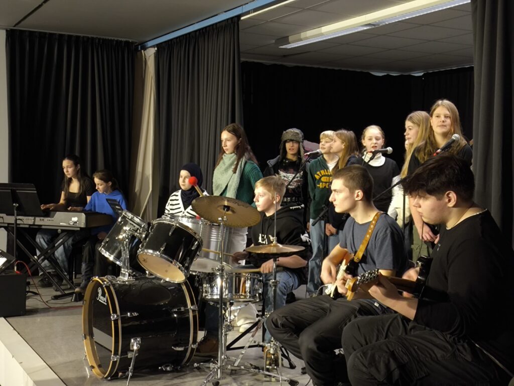 Schülergruppe mit Musikern und Sängerinnen auf einer Bühne.
