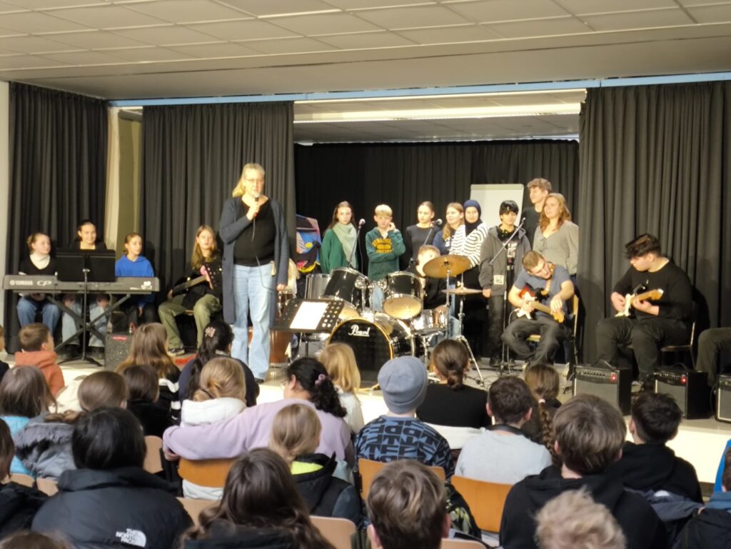 Schülerband spielt auf der Bühne vor einer großen Menge im Publikum.