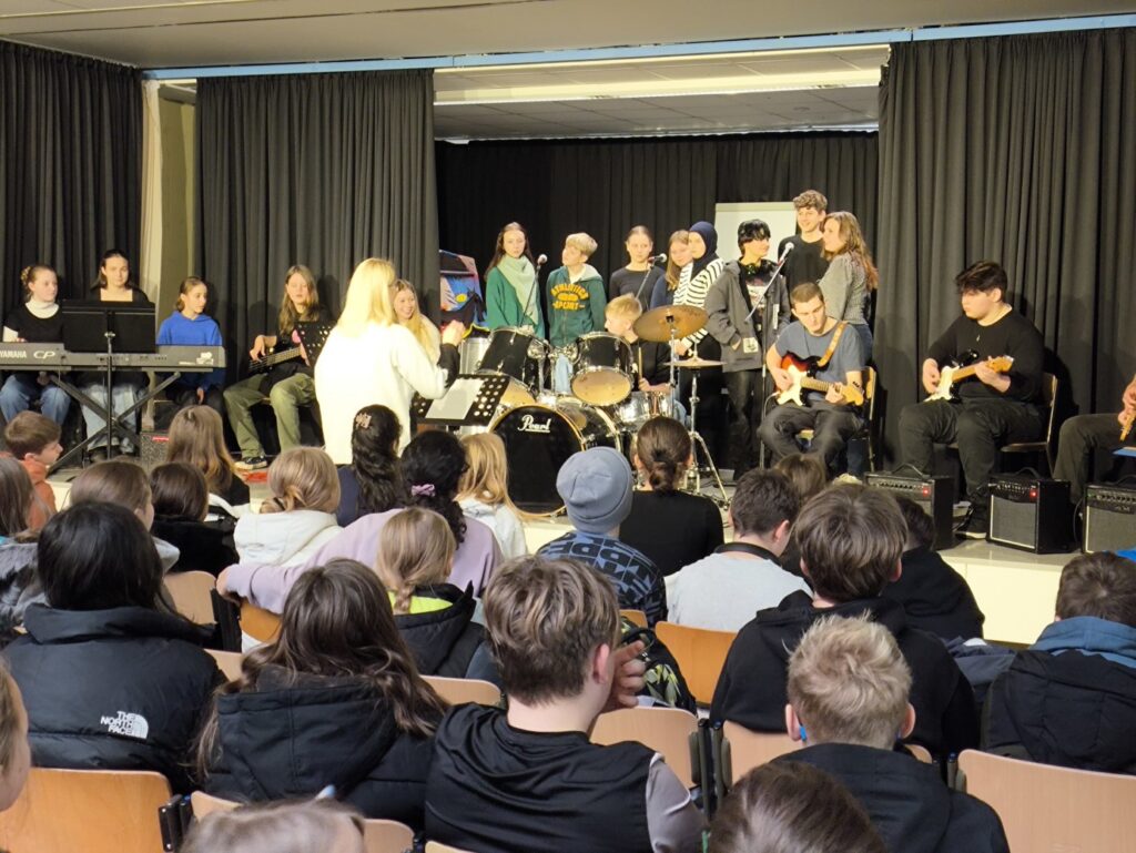 Schüler führen ein Musikstück live auf, mit Gesang und Instrumenten.