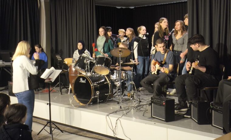 Schülerband spielt auf der Bühne, Sänger und Instrumentalisten sind aktiv.