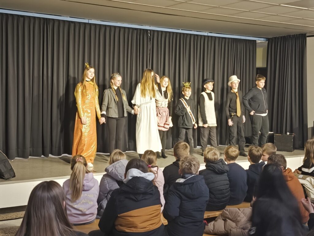 Schüler präsentieren ein Theaterstück auf der Bühne vor Publikum.