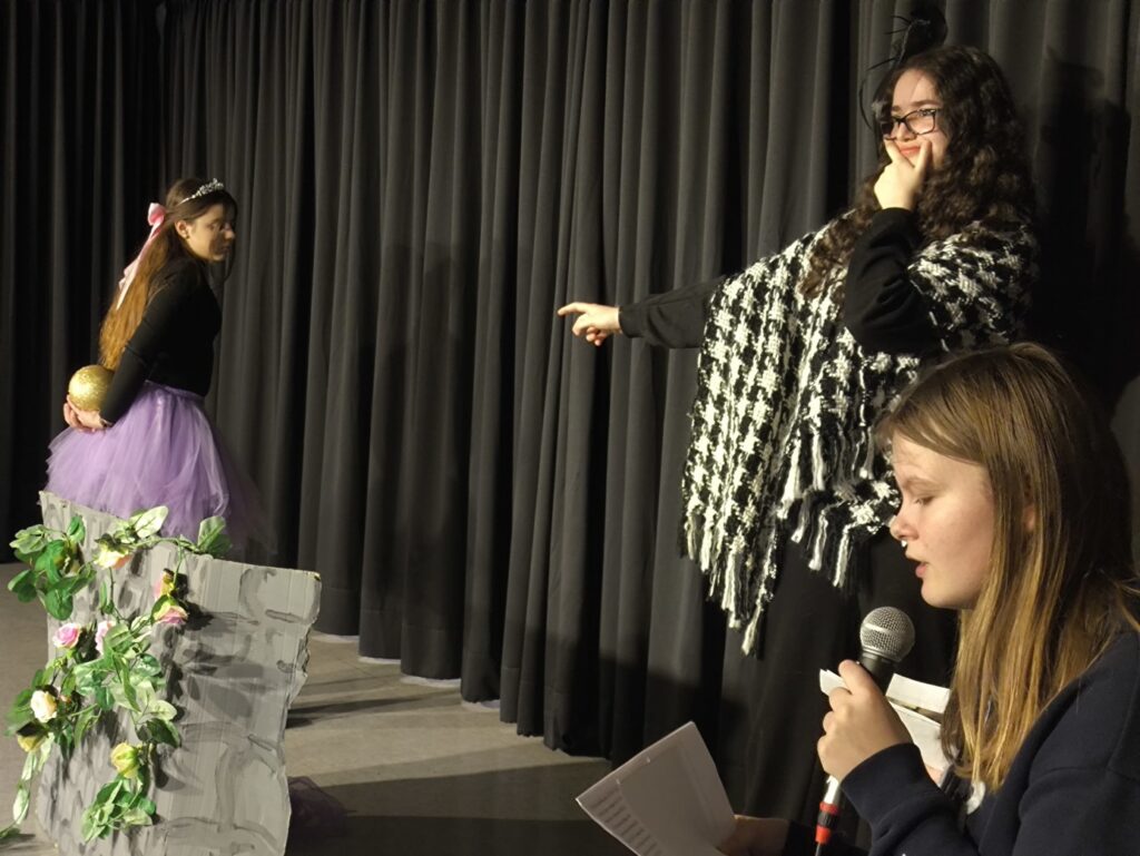 Zwei Schülerinnen führen auf einer Bühne ein Theaterstück auf.