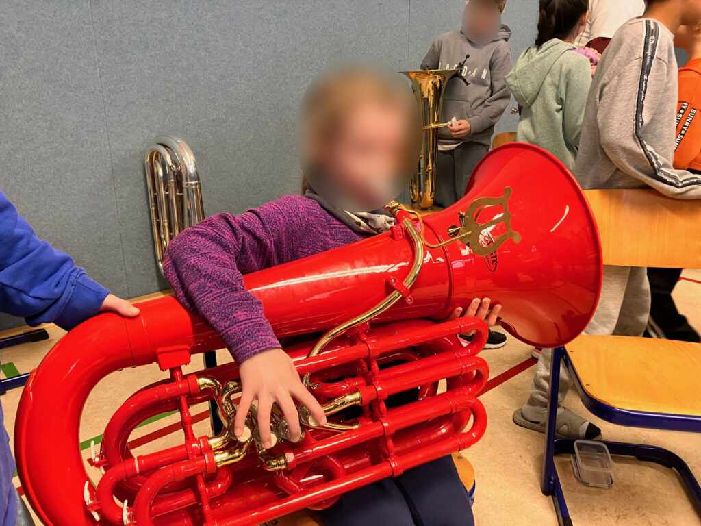 Kind spielt auf einer roten Tuba in einem Probenraum.