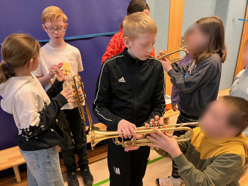 Schülerinnen und Schüler üben gemeinsam mit Trompeten in einem Klassenraum.