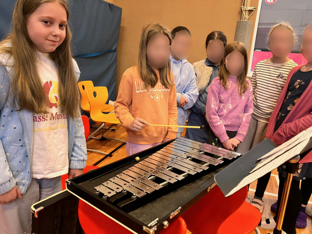 Schülerin spielt auf dem Xylophon, weitere Kinder stehen daneben.