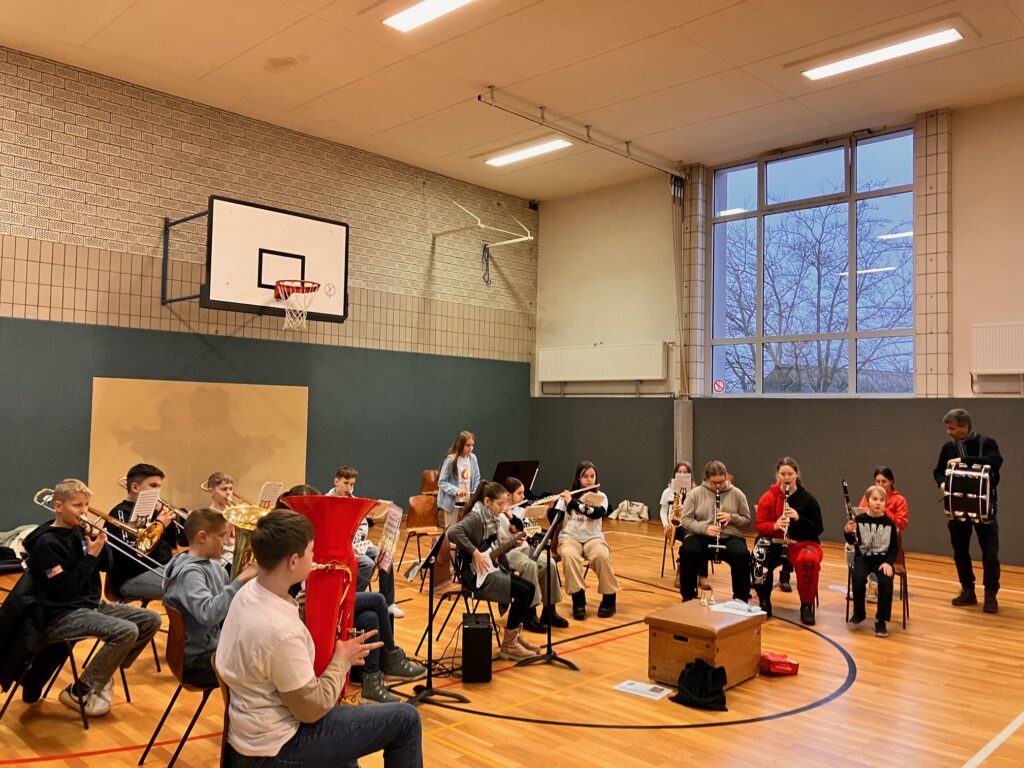 Schüler spielen in einer Turnhalle verschiedene Musikinstrumente.