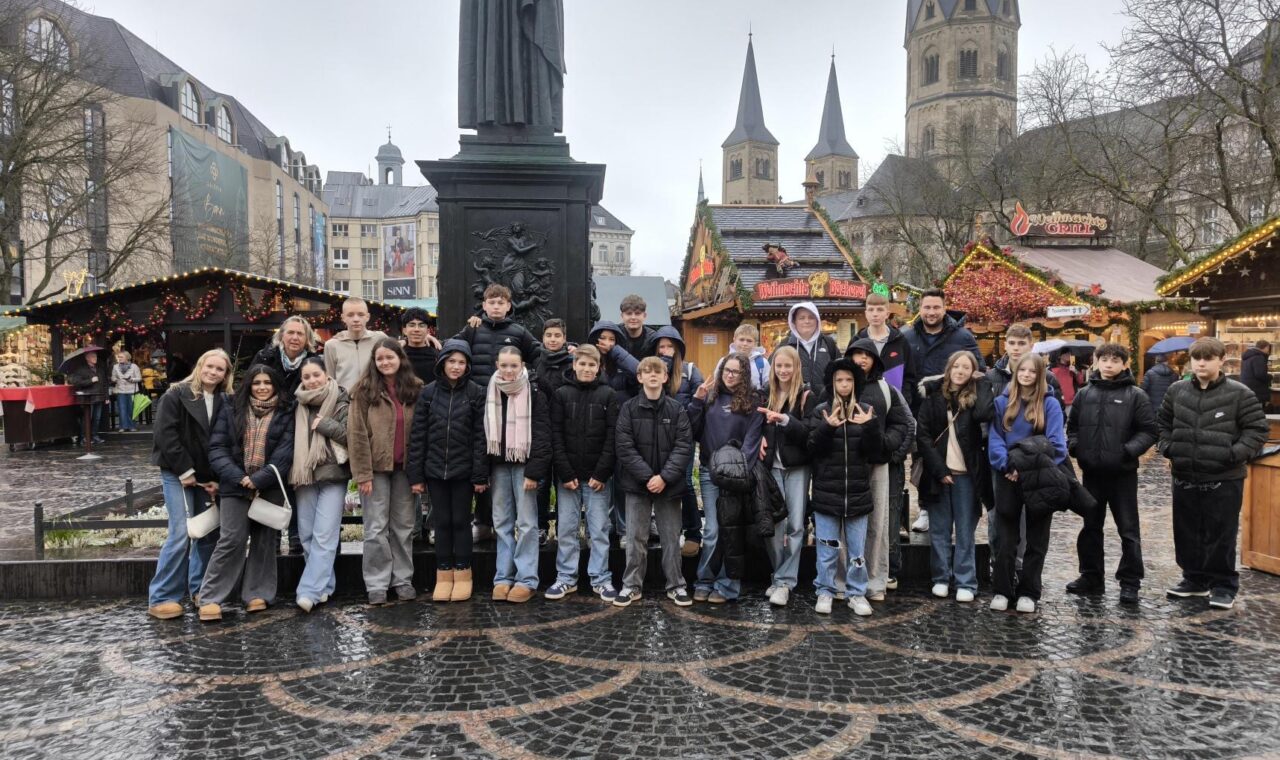 Gruppe von Personen vor einem Weihnachtsmarkt mit Ständen und einer Statue.