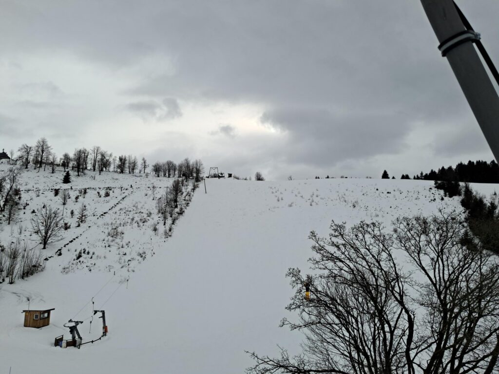 Schneebedeckte Piste mit Wolken und Skilift im Vordergrund.