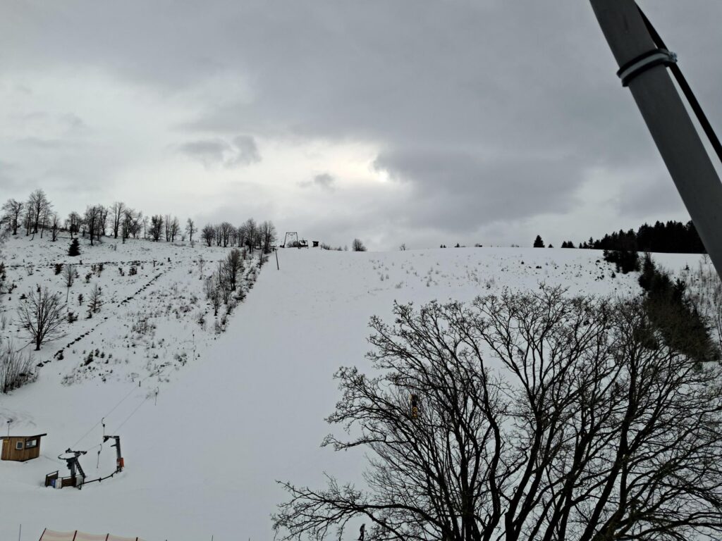 Winterszene mit schneebedecktem Hang und grauem Himmel.