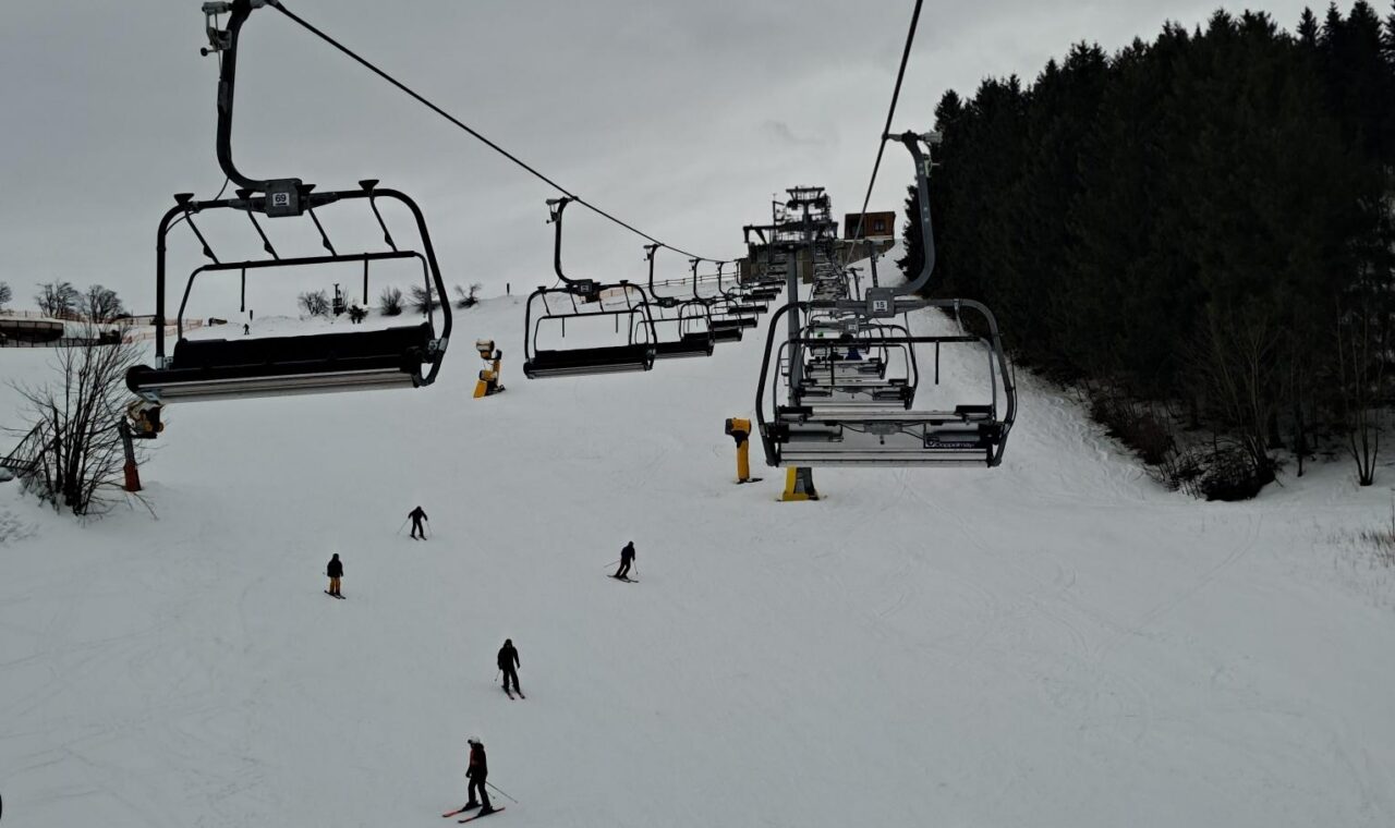 Skigebiet mit Sessellift und Skifahrern auf der Piste bei bewölktem Himmel.