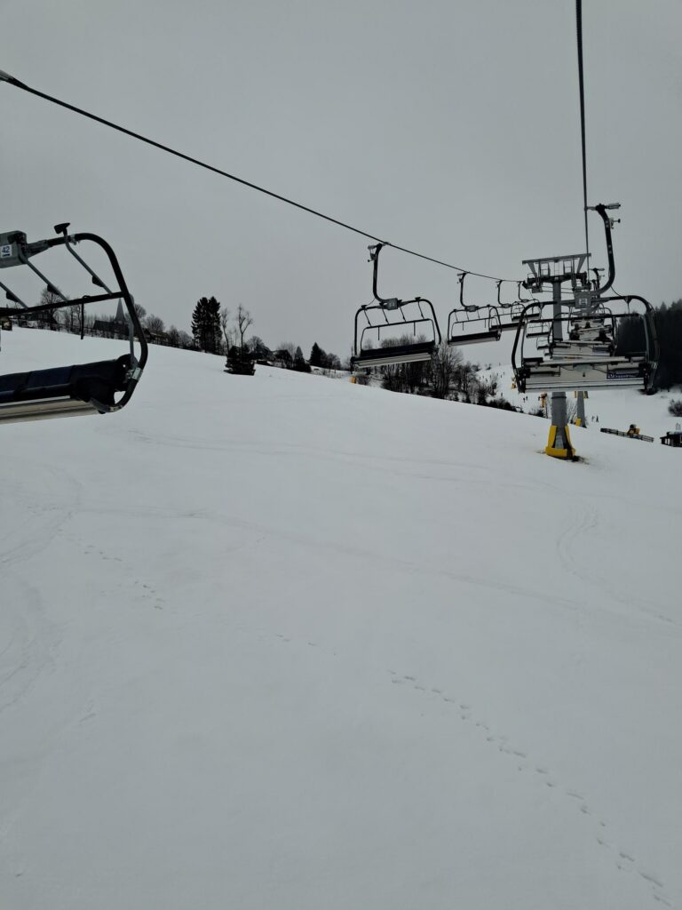 Skilift in verschneiter Landschaft, leere Sessellifte im Hintergrund.