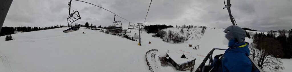 Skilift mit Besucher, schneebedeckte Landschaft und grauer Himmel.