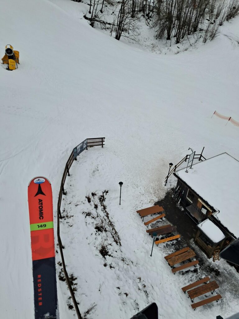 Blick auf eine verschneite Piste mit einer Skihütte und verschneiten Bänken.